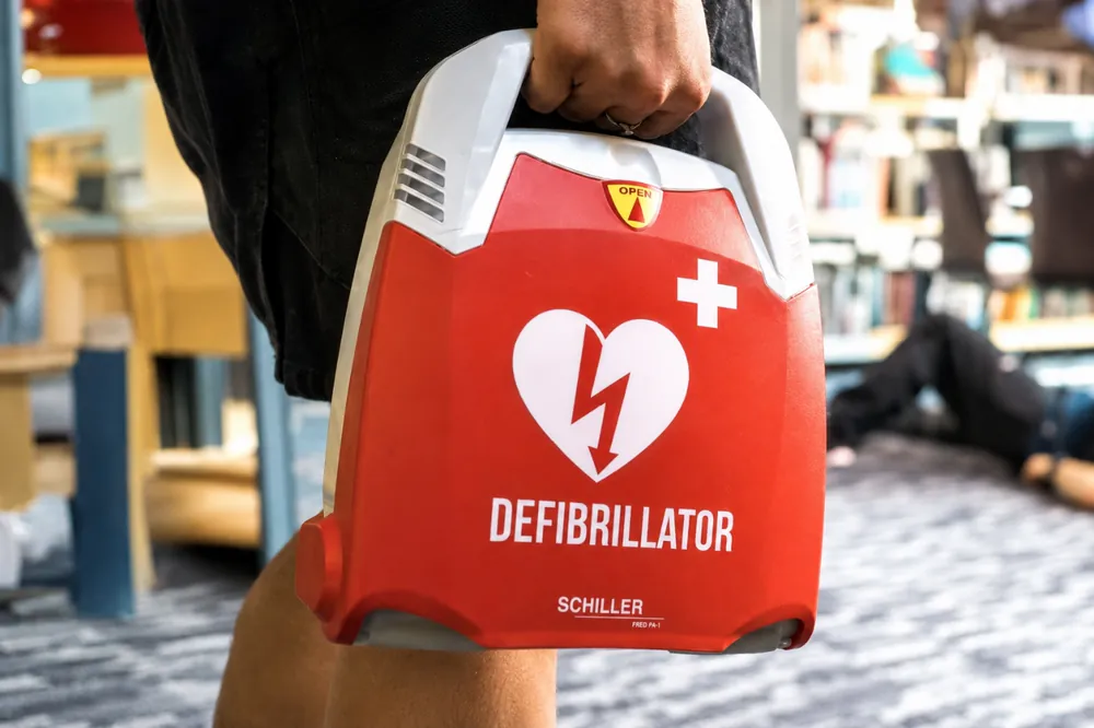 Desfibrilador Schiller FRED PA-1 sendo retirado do gabinete em um ambiente com circulação de público